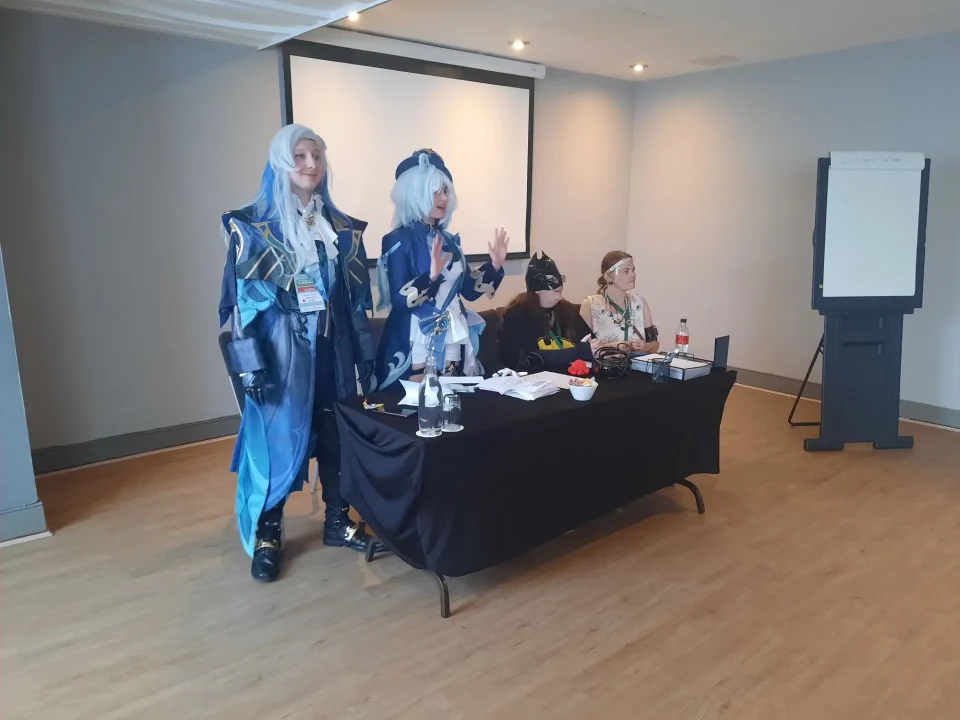 2025 Cosplay guests Fenek and Przysto stand next to a table. Kat and Karina are seated behind the table. They are all in cosplay.
